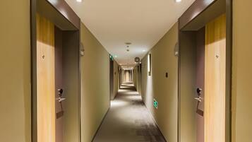 A hotel corridor with doors on both sides, a carpeted floor, and a ceiling with recessed lighting.