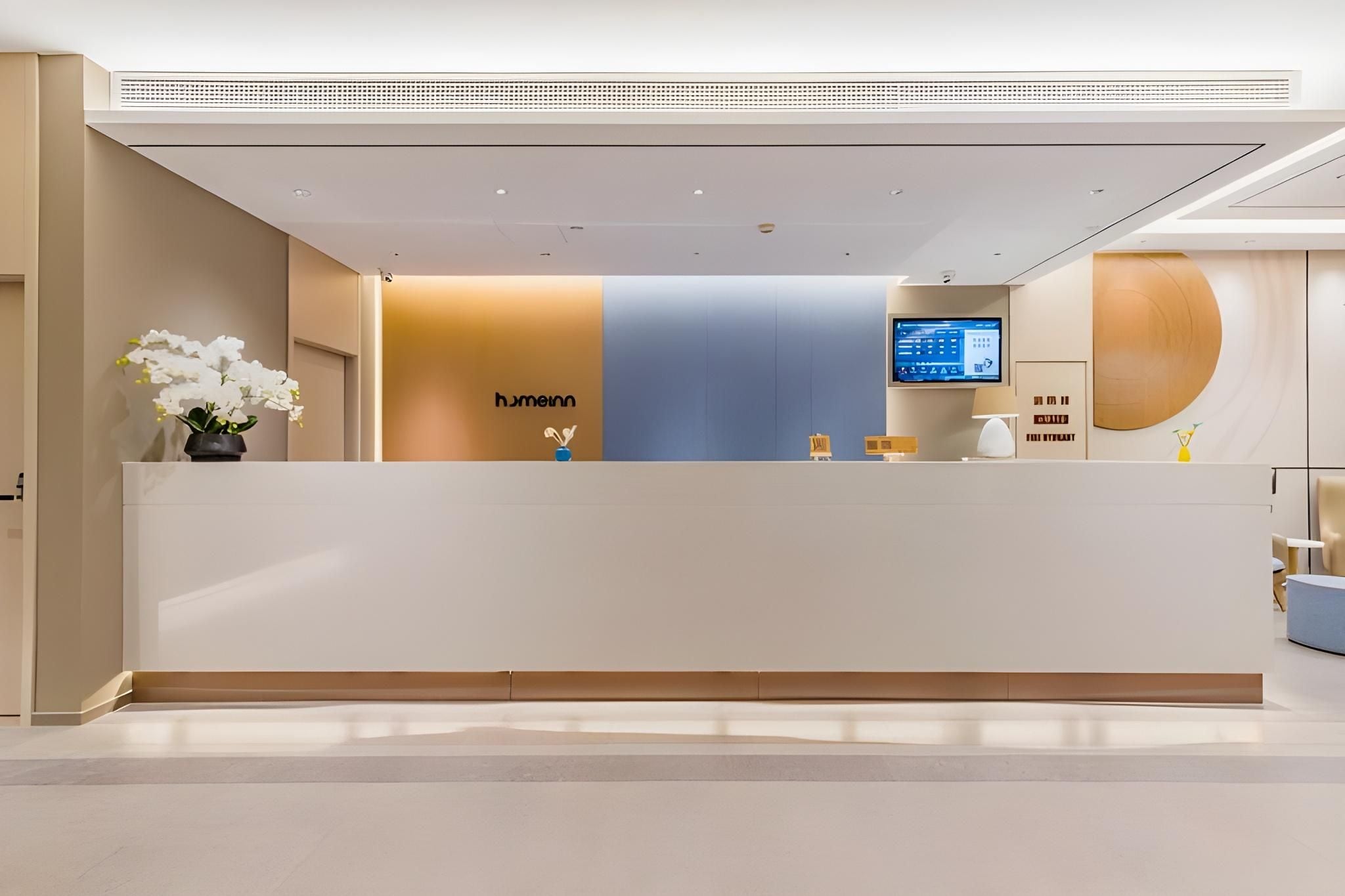 A reception desk with a modern design, a flat-screen monitor, and a potted plant.