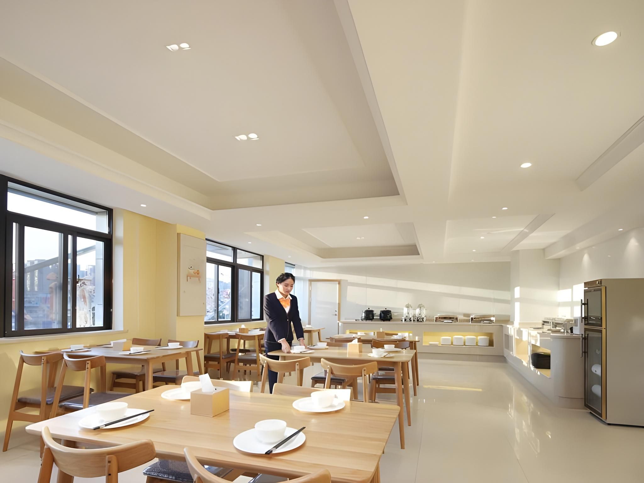 A modern dining area with wooden tables and chairs, a service area with a counter, and large windows providing natural light.