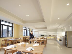 Un'area pranzo moderna con tavoli e sedie in legno, un angolo dedicato al servizio con un bancone, e ampie finestre che lasciano entrare luce naturale.