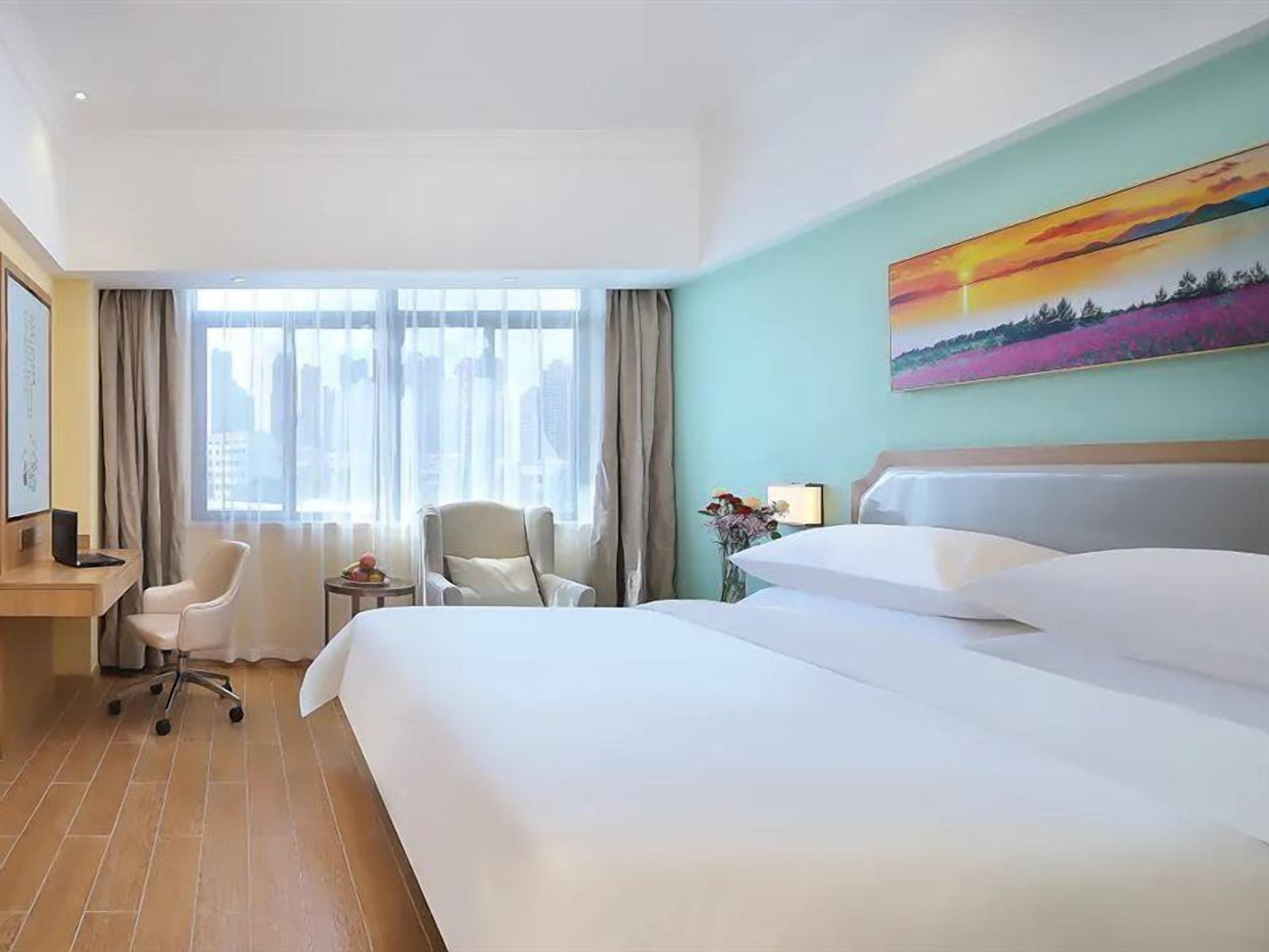 Una habitación de hotel con una cama grande, dos sillas, un escritorio y un ventanal con cortinas.