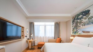 Quarto de hotel com uma cama grande, uma escrivaninha, uma televisão e um quadro na parede.
