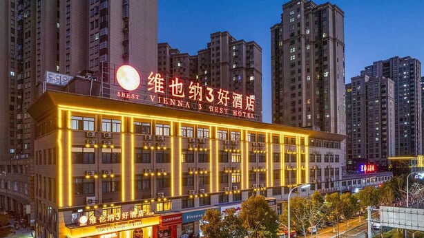 Um hotel com vários andares, fachada iluminada, restaurante no térreo e área de estacionamento.