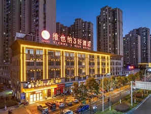 A multi-story hotel with illuminated signage, a ground-level restaurant, and a parking area.
