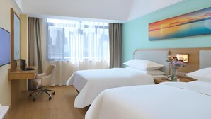 Quarto de hotel com duas camas, uma escrivaninha com cadeira, televisão e um quadro na parede.