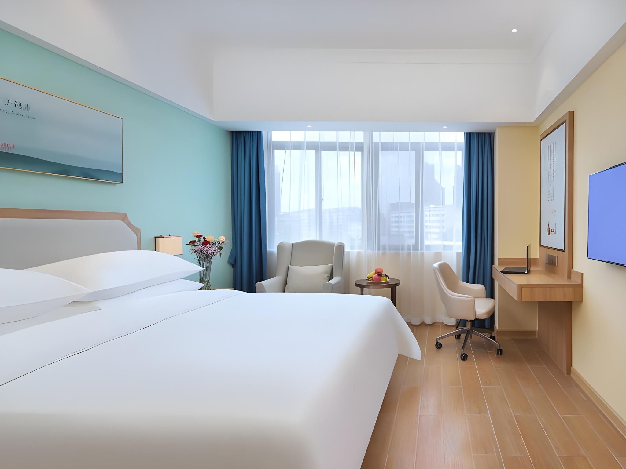 A hotel room with a bed, a desk, a chair, a TV, and a window with curtains.