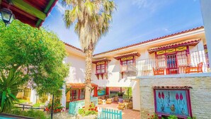 A courtyard with a palm tree, a stone wall, and a building with a balcony. - Zehra Tatil Koyu (Fethiye)