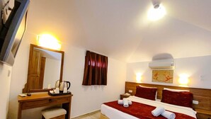 A hotel room with a bed, bedside table, lamp, and a desk with a mirror and a trash bin. - Zehra Tatil Koyu (Fethiye)
