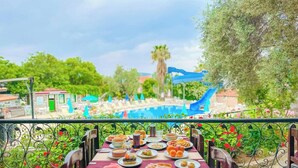 A dining table with a variety of dishes and a view of a pool area with a slide. - Zehra Tatil Koyu (Fethiye)