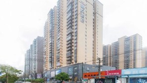Um edifício residencial alto com várias varandas, uma área comercial em primeiro plano e céu claro.