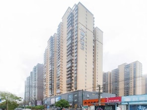Un edificio residencial de gran altura con varios balcones, una zona comercial en primer plano y un cielo despejado.