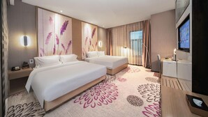 Quarto de hotel com duas camas, uma escrivaninha, televisão e uma janela grande com cortinas.