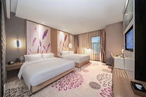 Habitación de hotel con dos camas, un escritorio, un televisor y un ventanal grande con cortinas.