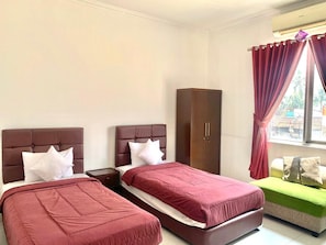 A hotel room with two beds, a wardrobe, and a window with curtains. - Charaka Hotel (Cibeleng)