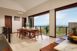 A dining area with a table set for four, a staircase, and a balcony with a view of the sea. - Kampi Villas by Premier Hospitality Asia (Nusa Dua)