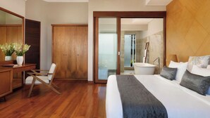 A modern hotel room with a large bed, a desk with a chair, a wardrobe, and a bathroom with a bathtub. - Kampi Villas by Premier Hospitality Asia (Nusa Dua)