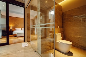 A modern bathroom with a glass shower enclosure, a toilet, and a visible bedroom with a bed and nightstand. - Kampi Villas by Premier Hospitality Asia (Nusa Dua)
