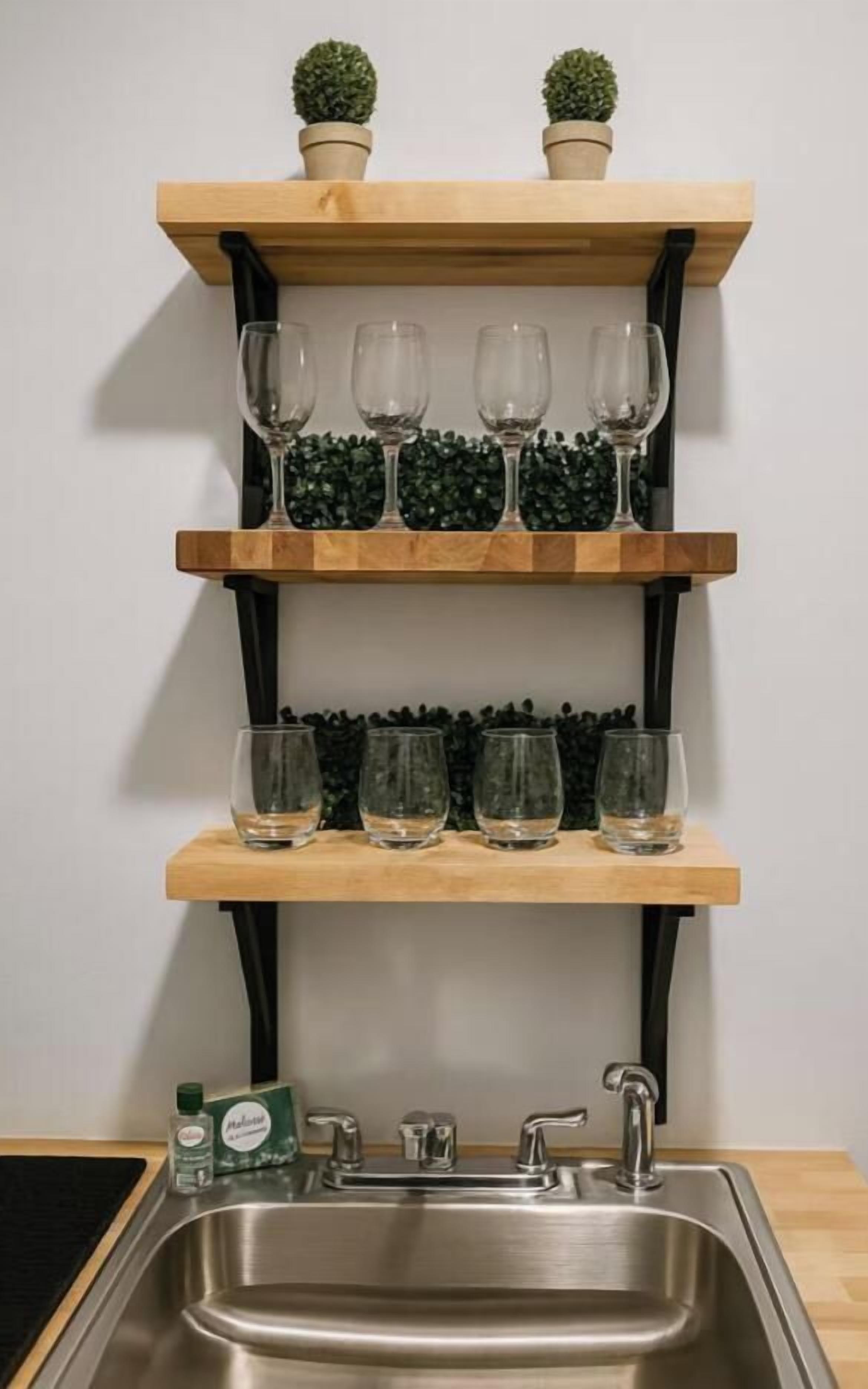 A kitchen with a stainless steel sink, wooden shelves with glasses, and potted plants.