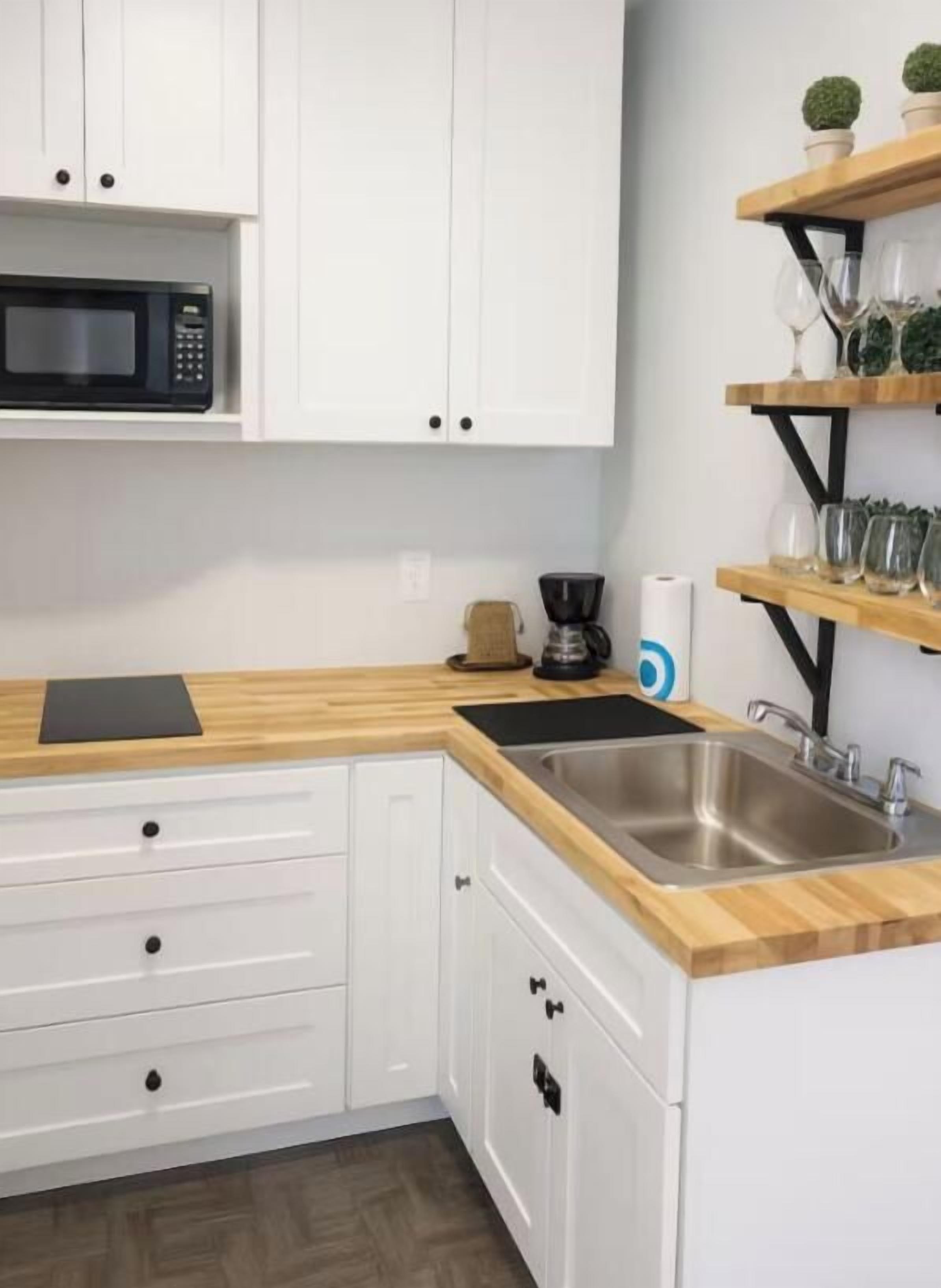 A kitchen with white cabinets, a wooden countertop, a stainless steel sink, a coffee maker, and a microwave.