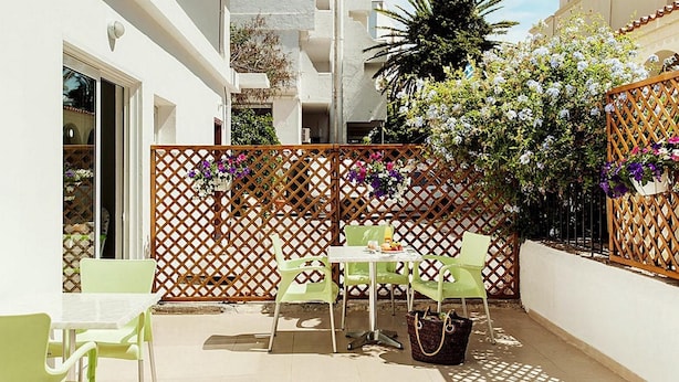 Patio esterno con tavolo e sedie, recinzione in legno e piante in vaso.