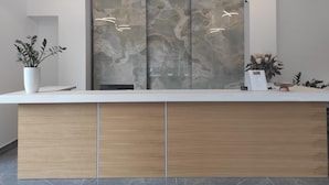 Una scrivania della reception con parete di fondo in marmo, due lampade a sospensione e piante in vaso.