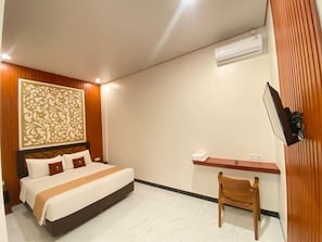 Una habitación de hotel con una cama, un escritorio, una silla, un televisor y un equipo de aire acondicionado.