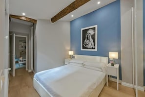 A bedroom with a large bed, two bedside tables with lamps, a framed picture on the wall, and a wooden ceiling beam. - Ponte Vecchio Deluxe (Florence)