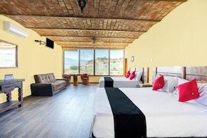 A hotel room with a brick ceiling, large windows, a sofa, a desk, and two beds with red pillows. - Collection O Hotel Monte Agave (Tequila)