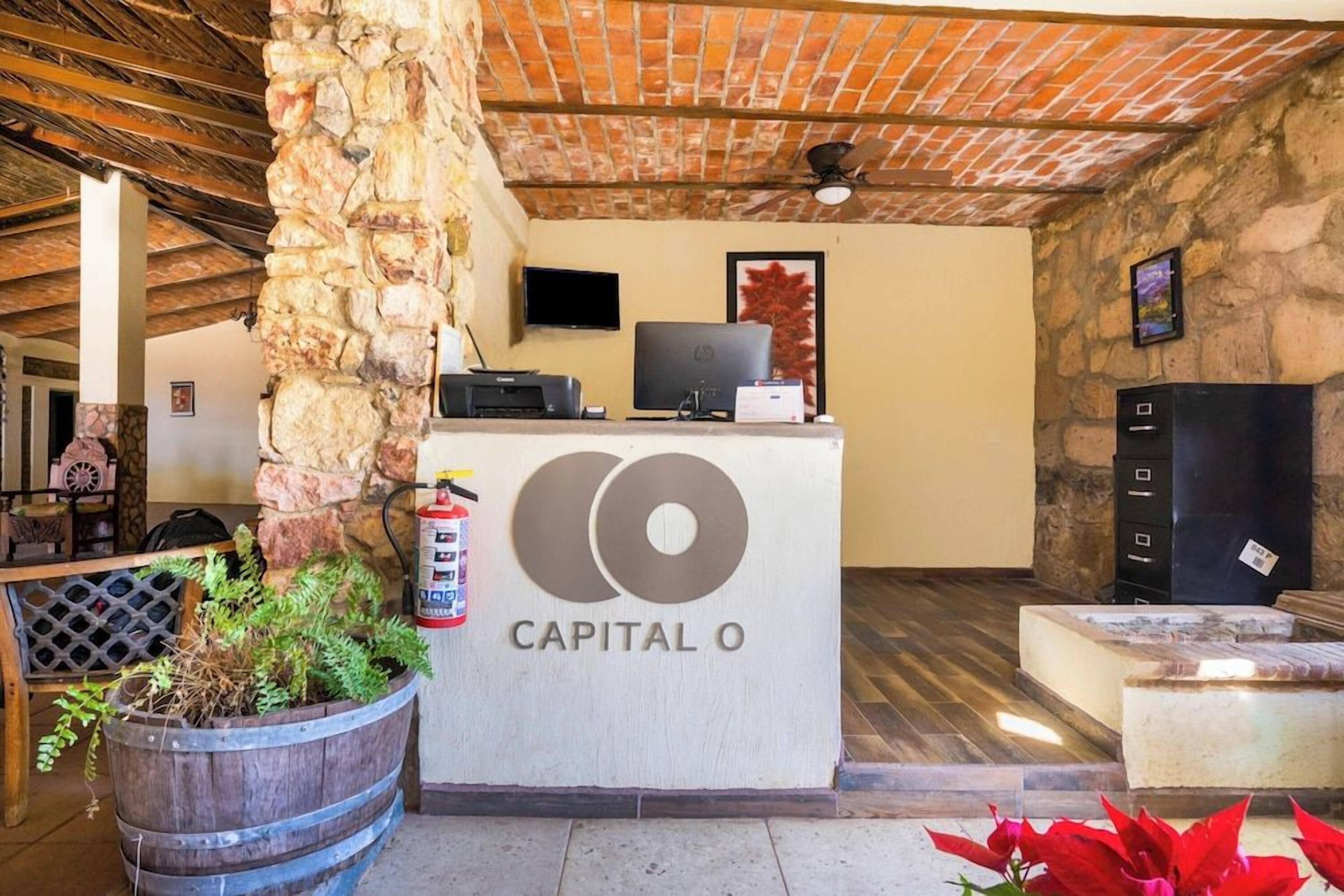 Un mostrador de recepción con un logotipo, un extintor, un televisor y un pilar de piedra.