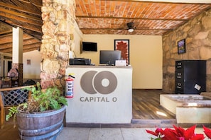 A reception desk with a logo, a fire extinguisher, a television, and a stone pillar. - Collection O Hotel Monte Agave (Tequila)