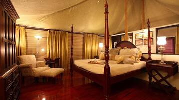 A four-poster bed with a canopy, a wooden dresser, a chair, and a bedside table with a lamp.
