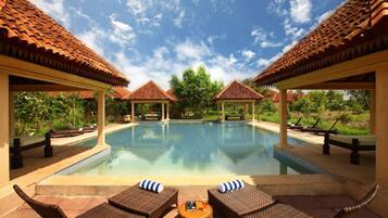 A pool area with lounge chairs and umbrellas, surrounded by covered structures with tiled roofs.
