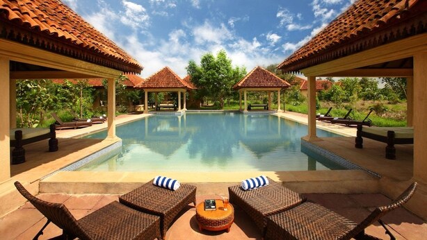 A pool area with lounge chairs and umbrellas, surrounded by covered structures with tiled roofs. - Tuli Tiger Corridor (Barghat)