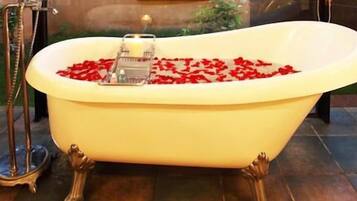 A bathtub filled with red rose petals and a candle, with a metal stand beside it.