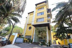 A multi-story building with a yellow facade, a visible entrance, and a sign indicating a zip code. - Zip by Spree Hotels Hyde (Candolim)