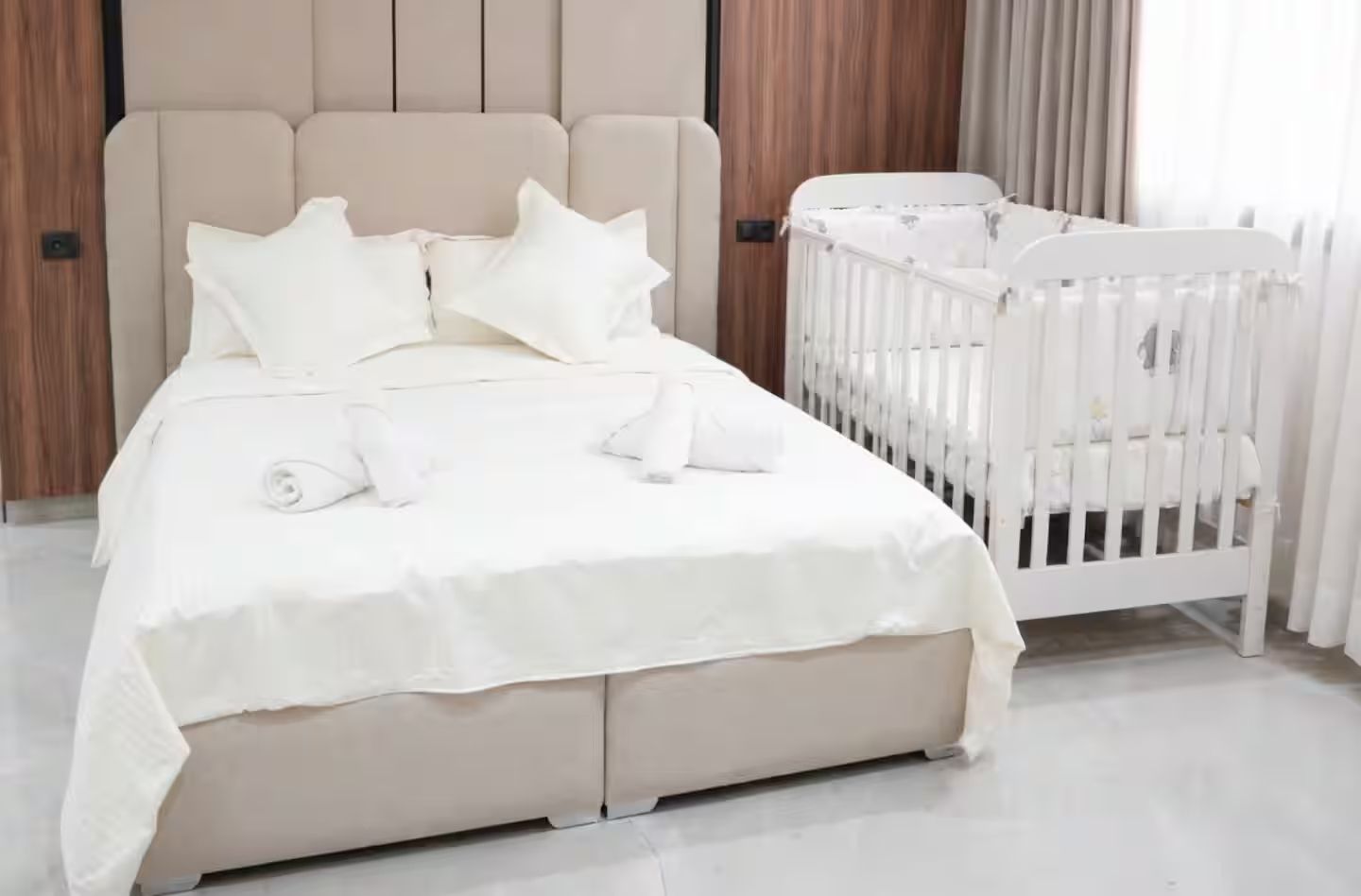 Quarto com cama, almofadas, berço e cabeceira de madeira.