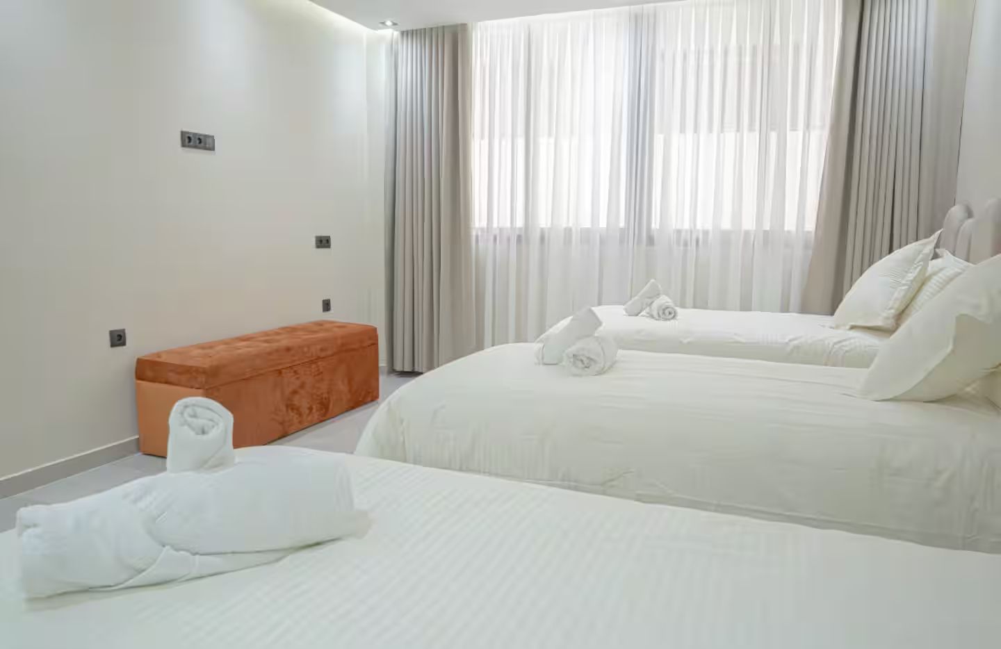 Une chambre d’hôtel avec deux lits, un banc et une fenêtre avec des rideaux.