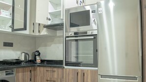 Una cocina equipada con microondas, horno y refrigerador. Hay una cafetera y un hervidor sobre la encimera.