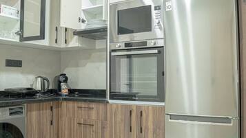 Cozinha equipada com micro-ondas, forno e frigorífico. Há uma máquina de café e uma chaleira no balcão.