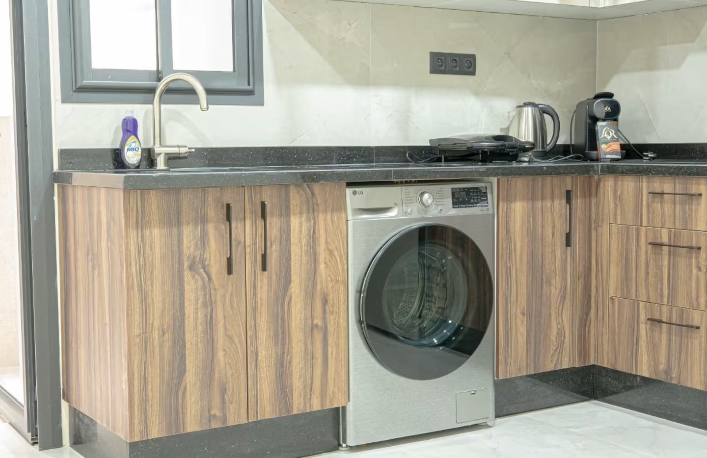 Une cuisine moderne équipée d’un lave-linge encastré, d’une machine à café et d’une bouilloire posées sur le plan de travail.