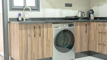 Une cuisine moderne équipée d’un lave-linge encastré, d’une machine à café et d’une bouilloire posées sur le plan de travail.