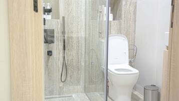 Ein modernes Badezimmer mit einer Duschkabine aus Glas, einer weißen Toilette und einem Mülleimer.