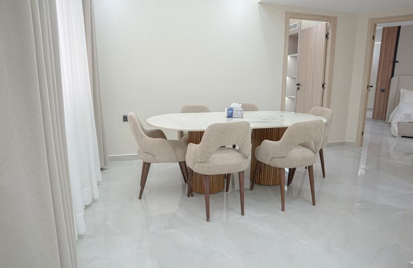 Un coin repas avec une table ronde et six chaises, une boîte de mouchoirs posée sur la table et un sol blanc.
