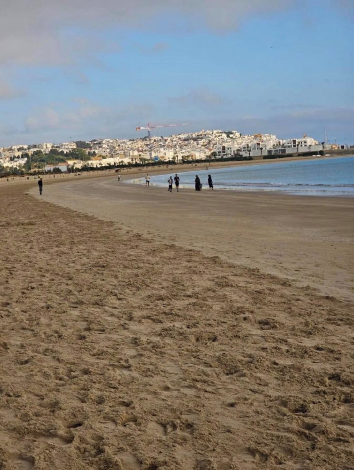 Uma extensa praia de areia com vista clara para uma vila costeira ao fundo.