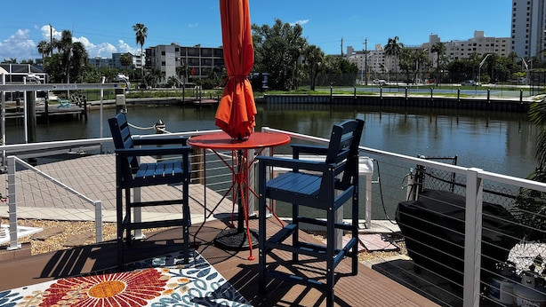Eine Terrasse mit Tisch und Stühlen mit Blick auf ein Gewässer und Gebäude im Hintergrund.