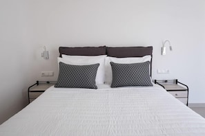 A bed with a white quilt, two patterned pillows, and a headboard. - Santoterra Antigua Luxury Suites (Santorini)