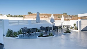 Un área de patio al aire libre con mesas, sillas, sombrillas y plantas en macetas.