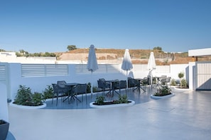 Eine Außenpatio-Terrasse mit Tischen, Stühlen, Sonnenschirmen und Topfpflanzen.