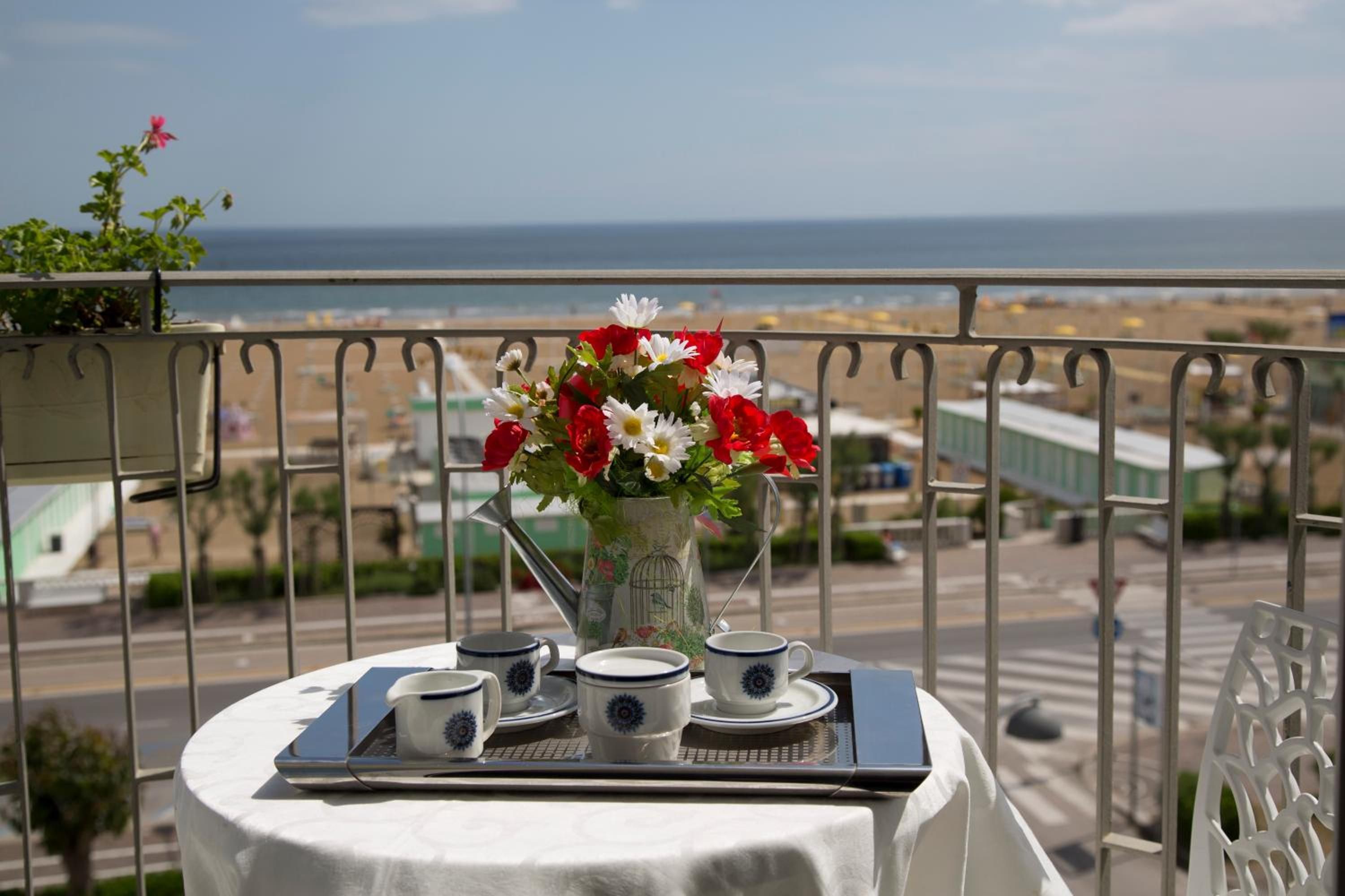 A balcony with a table set for tea, a vase of flowers, and a view of the sea.