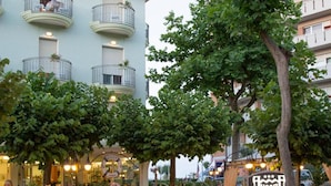 Un hotel con fachada azul claro, varios balcones y un área de café a nivel de la calle con mesas al aire libre.